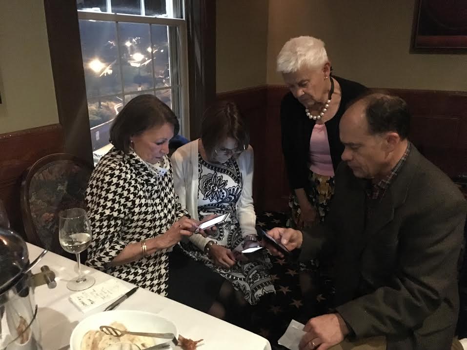 A group of people look at their phones while sitting at a table