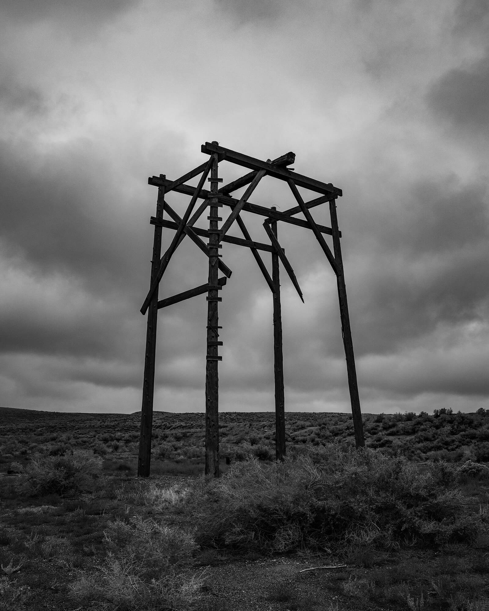 the black skeleton of an abandoned oil derrick in an empty field on a cloudy day