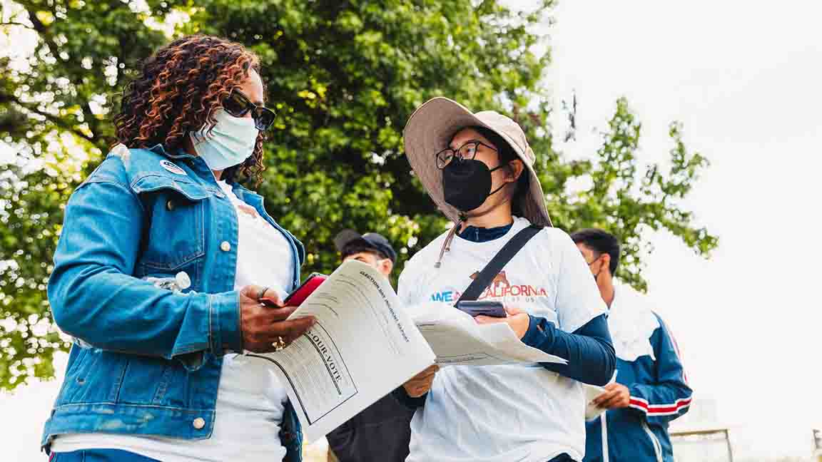 Two people wearing masks outdoors discussing the election