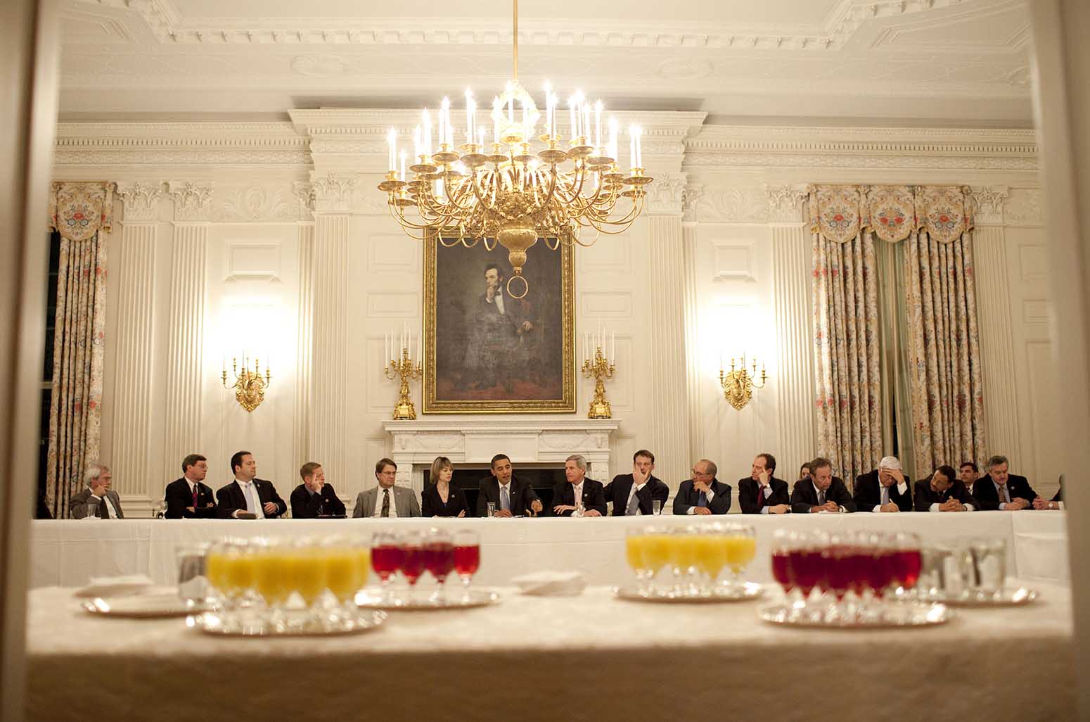 Feb. 10, 2009 “The President meets with the Democratic Blue Dog coalition in the State Dining Room. I had noticed the glasses of cranberry and orange juice sitting on a table in the doorway of the Red Room, so I backtracked to compose this picture from inside the Red Room.” (Official White House photo by Pete Souza)